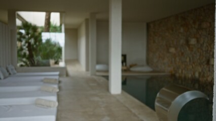 Spa interior with blurred loungers and defocused pool area featuring stone wall, creating a serene wellness ambiance perfect for relaxation and rejuvenation.