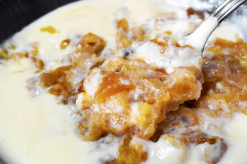 Apple crumble with custard on spoon in a bowl.