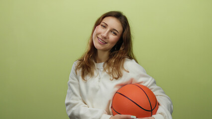 Woman holding basketball against a yellow background smiles warmly, capturing the essence of youth,...