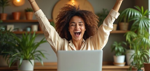 Happy biracial woman uses laptop celebrating winning online contest prize. Cheerful female with raised arms feels excited, happy after success, win. Woman smiles, laughs with joy. Home interior with
