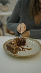 Woman enjoying dessert at luxurious restaurant indoors with modern coffeehouse ambiance eating chocolate cake with fork in elegant setting.