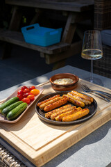 Delicious grilled sausages served on a black plate with cherry tomatoes, mini cucumbers, dipping...