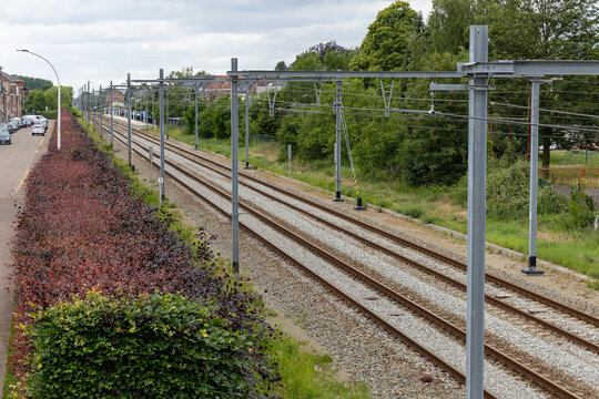 Editorial image of a railway line running through a suburban area, featuring multiple tracks, power poles, green vegetation and houses with solar panels in the background.