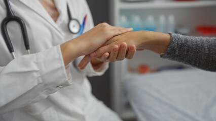 Doctor holding patient's hand in a clinic room, showing care and support during a medical...