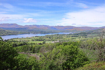 Picturesque view of Lake Windermere and the rolling hills of the Lake District, England, under a vivid spring sky.