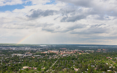 The dramatic sky and rainbow create a breathtaking contrast above Boulder, capturing the peaceful harmony between nature and urban life.