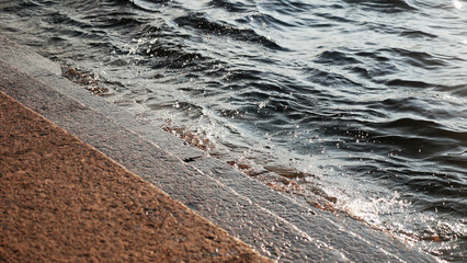 Waves break on granite steps, splashes in the rays of the sun