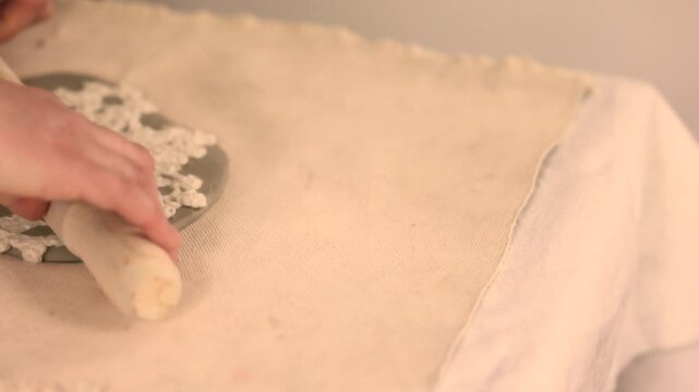 Handcrafting ceramic Christmas decorations in a pottery studio. Using fabric snowflake stencil and rolling pin to imprint festive patterns on clay. Creative and cozy holiday preparation.