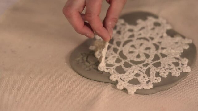 Handcrafting ceramic Christmas decorations in a pottery studio. Using fabric snowflake stencil and rolling pin to imprint festive patterns on clay. Creative and cozy holiday preparation.