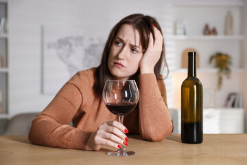 Alcohol addiction. Miserable woman with wine at table indoors