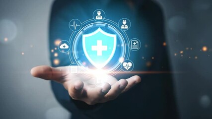 A hand holding a shield with a white cross and medical icons surrounding it in a digital display - Powered by Adobe