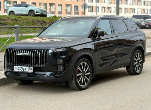 A modern black Jaecoo J7 luxury crossover car parked on a city street pavement against contemporary residential buildings.