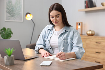 Beautiful woman with planner making notes at wooden table indoors