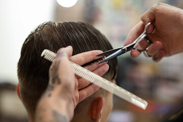 Professional barber cutting client's hair with scissors in barbershop, closeup