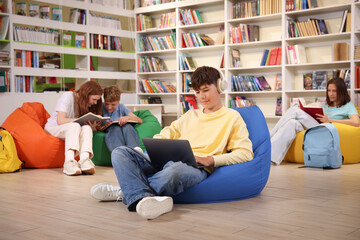 Student with laptop studying on bean bag in library