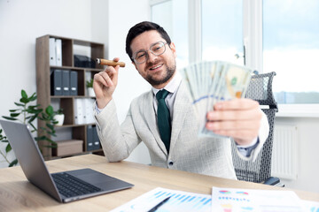 Happy greedy banker with dollar banknotes and cigar at table in office, selective focus