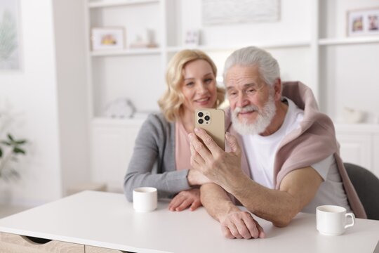 Senior man and mature woman watching something on smartphone at home, selective focus. Happy couple - Powered by Adobe