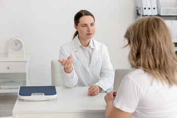 Fototapeta premium Weight loss. Nutritionist consulting overweight woman at white desk in clinic