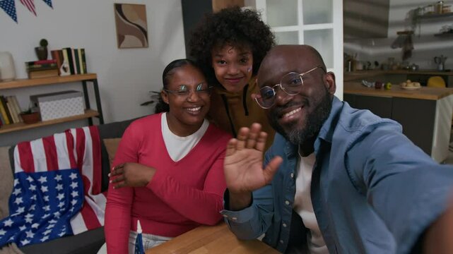 UGC shot of Black family smiling and waving at camera when recording video for social media during Fourth of July home party
