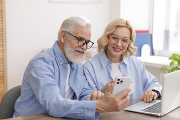 Senior man and mature woman watching something on smartphone at home. Happy couple