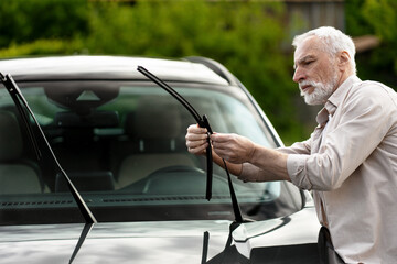 Senior man replacing windshield wiper blade on car