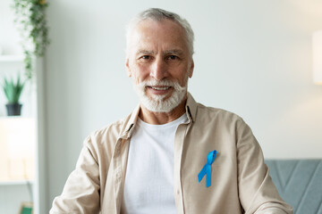 Senior man wearing blue ribbon is smiling at home