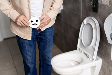 Man suffering abdominal pain in the toilet holding a sad face