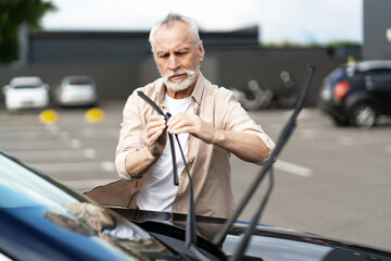 Senior man replacing windshield wipers on his car in parking lot