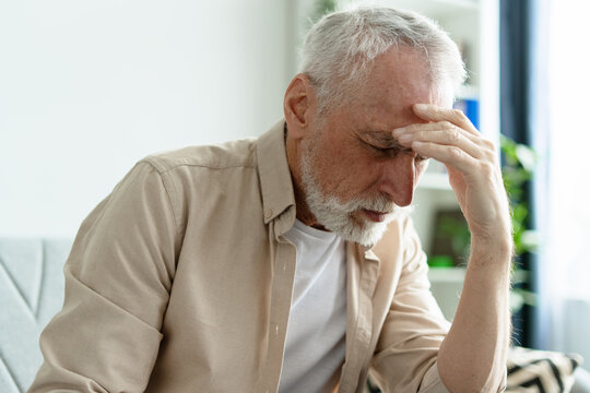 Worried senior man suffering from headache touching forehead at home - Powered by Adobe