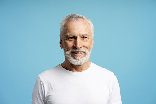Portrait of smiling senior man with white beard wearing white t shirt on blue background