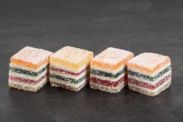 Layered multicolored jelly marmalade in the shape of a cube. Dark background. Copy space