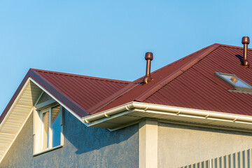 The striking red metal roof features multiple ventilation pipes, with a backdrop of a clear blue sky illuminating the structure during daylight hours