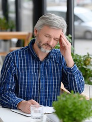 Stressed Man With Headache at Cafe Table, Illustrating Burnout and Mental Health Awareness in the Workplace, Seeking Employee Wellness Solutions : Generative AI