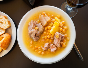 Plate with portion of hot chickpea and meat soup. First course is served with pieces of baguette..