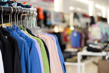 Sweatshirts of different colors hang on hangers on rack in clothing store