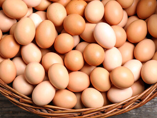 A woven basket overflowing with brown eggs sits atop a wooden table, highlighting a simple, rustic kitchen scene.