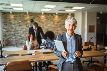 pretty aged businesswoman hold laptop in arms and smile at workplace
