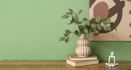 Vase with eucalyptus branches and books on table near green wall. Banner for design