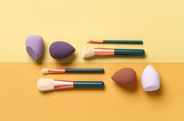Makeup sponges and brushes on yellow background