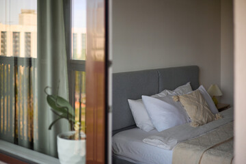 Cozy bedroom interior, beige bedspread and pillow, bedside lamp next to the bed, light from the window
