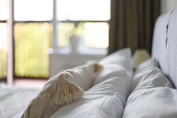 Cozy bedroom interior, beige bedspread and pillow, bedside lamp next to the bed, light from the window