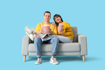Young couple in love with popcorn sitting on sofa against blue background