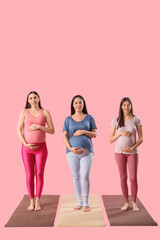 Fototapeta premium Beautiful young sporty pregnant women practicing yoga on pink background