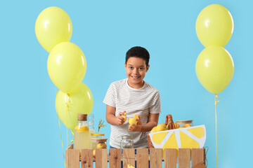 Little African-American boy squeezing lemon at lemonade stand on blue background