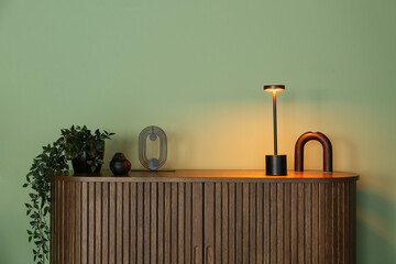 Wooden chest of drawers with glowing lamp near green wall