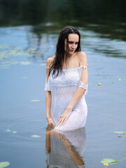 Young beautiful brunette woman in white dress posing in river with water lilies.