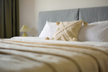 Cozy bedroom interior, beige bedspread and pillow, bedside lamp next to the bed, light from the window