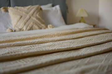 Cozy bedroom interior, beige bedspread and pillow, bedside lamp next to the bed, light from the window