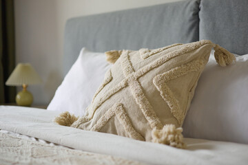 Cozy bedroom interior, beige bedspread and pillow, bedside lamp next to the bed, light from the window