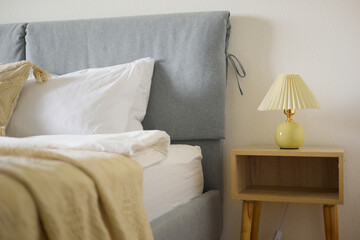 Cozy bedroom interior, beige bedspread and pillow, bedside lamp next to the bed, light from the window